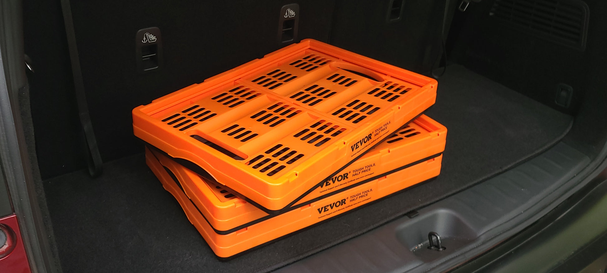 Collapsible storage crates folded flat and stacked in a vehicle trunk, top crate showing the slotted design