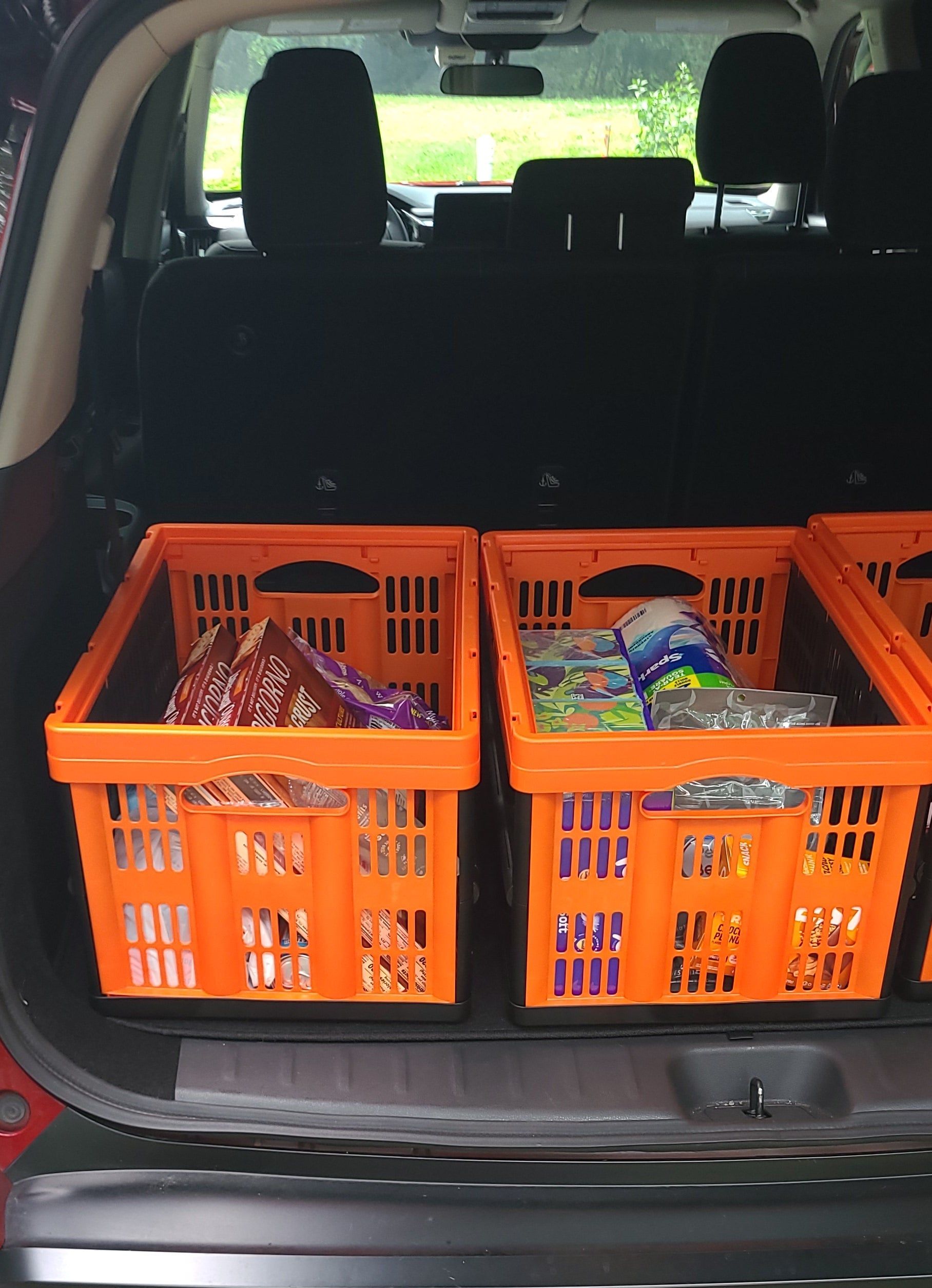 Two orange plastic collapsible utility crates stacked inside the open trunk of a red car.